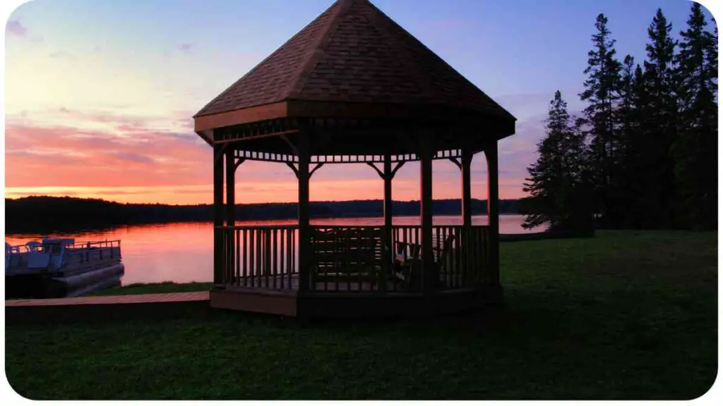 a gazebo on the shore of a lake at sunset