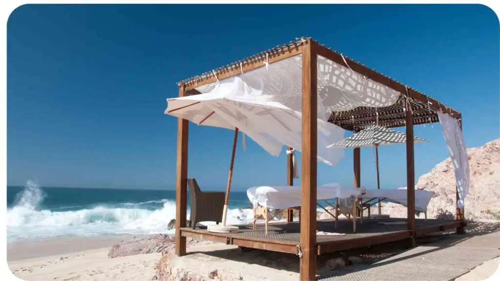 a gazebo on the beach with white sheets and umbrellas