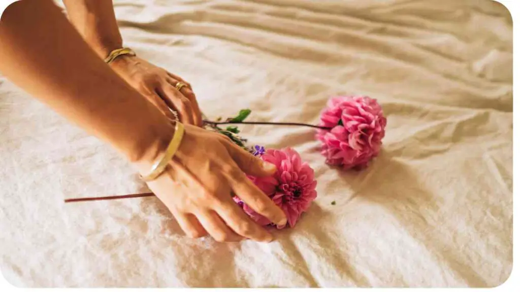 a person's hands are holding pink flowers on a bed