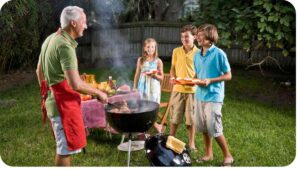 an older person grilling food with children in the yard