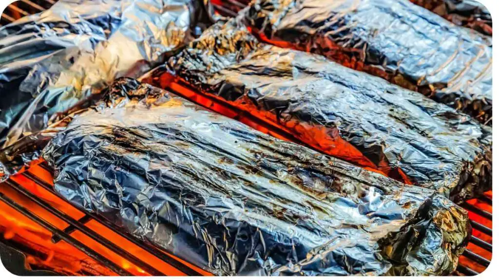 several pieces of meat wrapped in foil on an outdoor grill